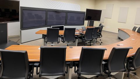 Virtual conferencing room with curved tables, multiple chairs and multiple monitors