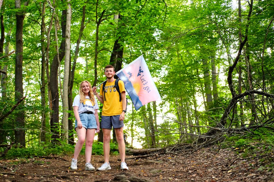 Two people holding a "Let's Go." flag while hiking in the woods
