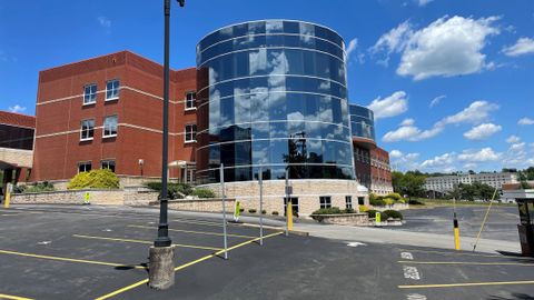 View of the left-front of the exterior building and parking lot, with windows reflecting the sunny sky