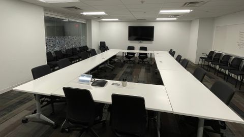 Large meeting room with tables forming a square and lots of chairs facing a tv monitor